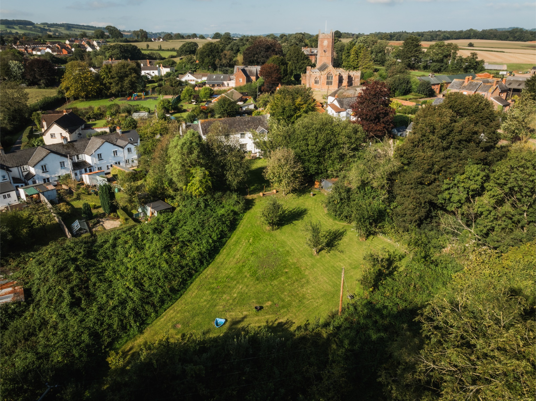 Aerial view over Paddock House’s lawns and mature trees towards Halberton church and the countryside