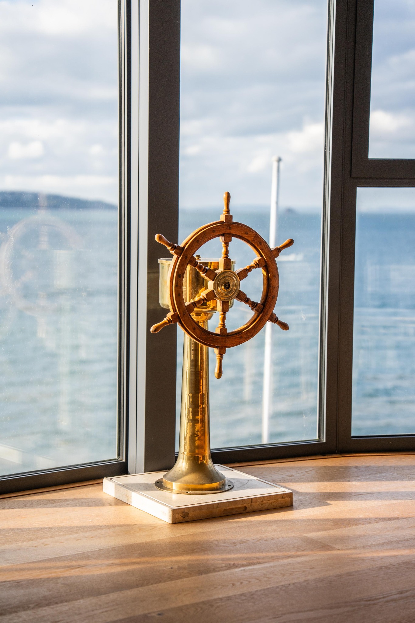 A decorative ship’s wheel beside a window overlooking the sea